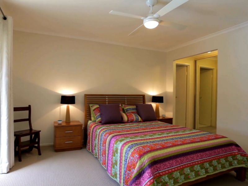 prikaz spavaće sobe sa šarenom posteljinom na krevetu, polica na kojoj je lampa i stolica u ćošku